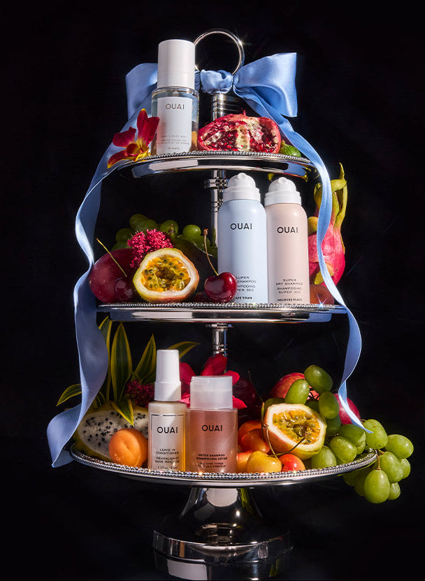 Three-tiered tray with OUAI hair care products and fruits on a black background