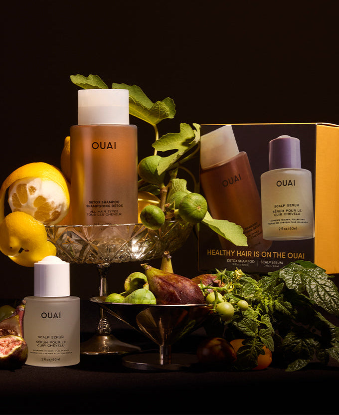 OUAI hair care products with greenery and decorative elements on a dark background