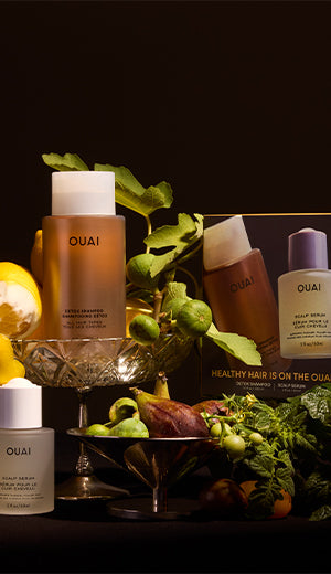 OUAI hair care products with greenery and fruits on a dark background