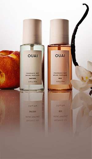 Two OUAI perfume bottles on a reflective surface with a vanilla bean and peach in the background.
